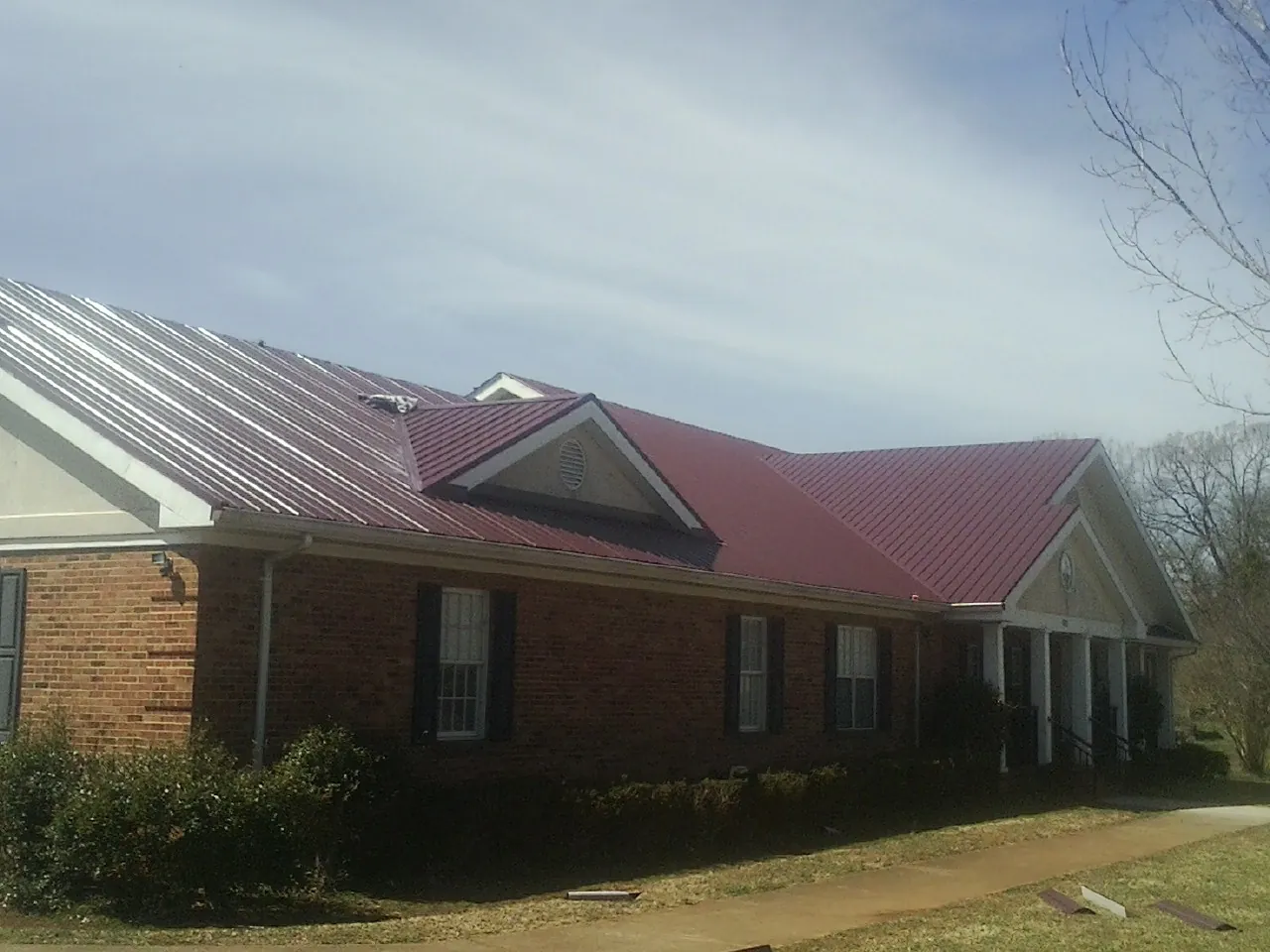 Red metal roof with gabled entries on a long brick building, from a Hail Damage Roof Repair job in Mc Kees Rocks