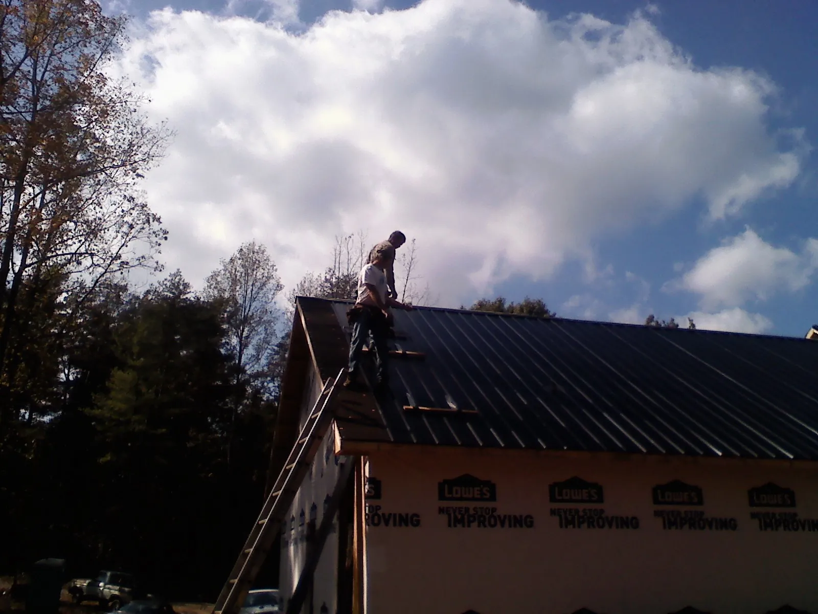 Roofer fastening dark metal panels high against a cloudy sky, from a Roof Inspection job in Mc Kees Rocks